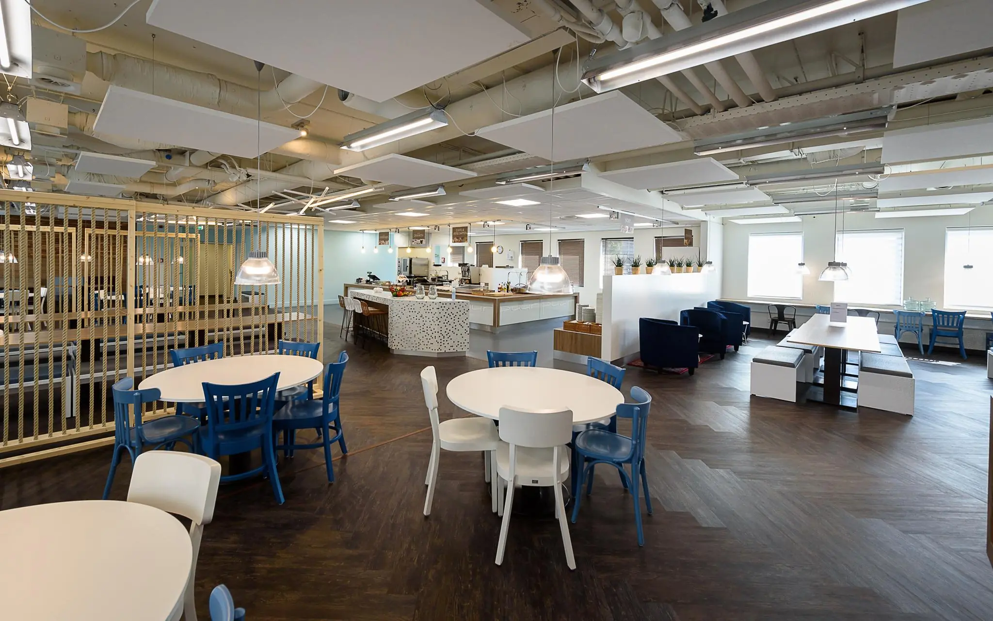 Moderne bedrijfskantine aan het Rivium Boulevard met ronde tafels, een open keuken en diverse zitgedeeltes.